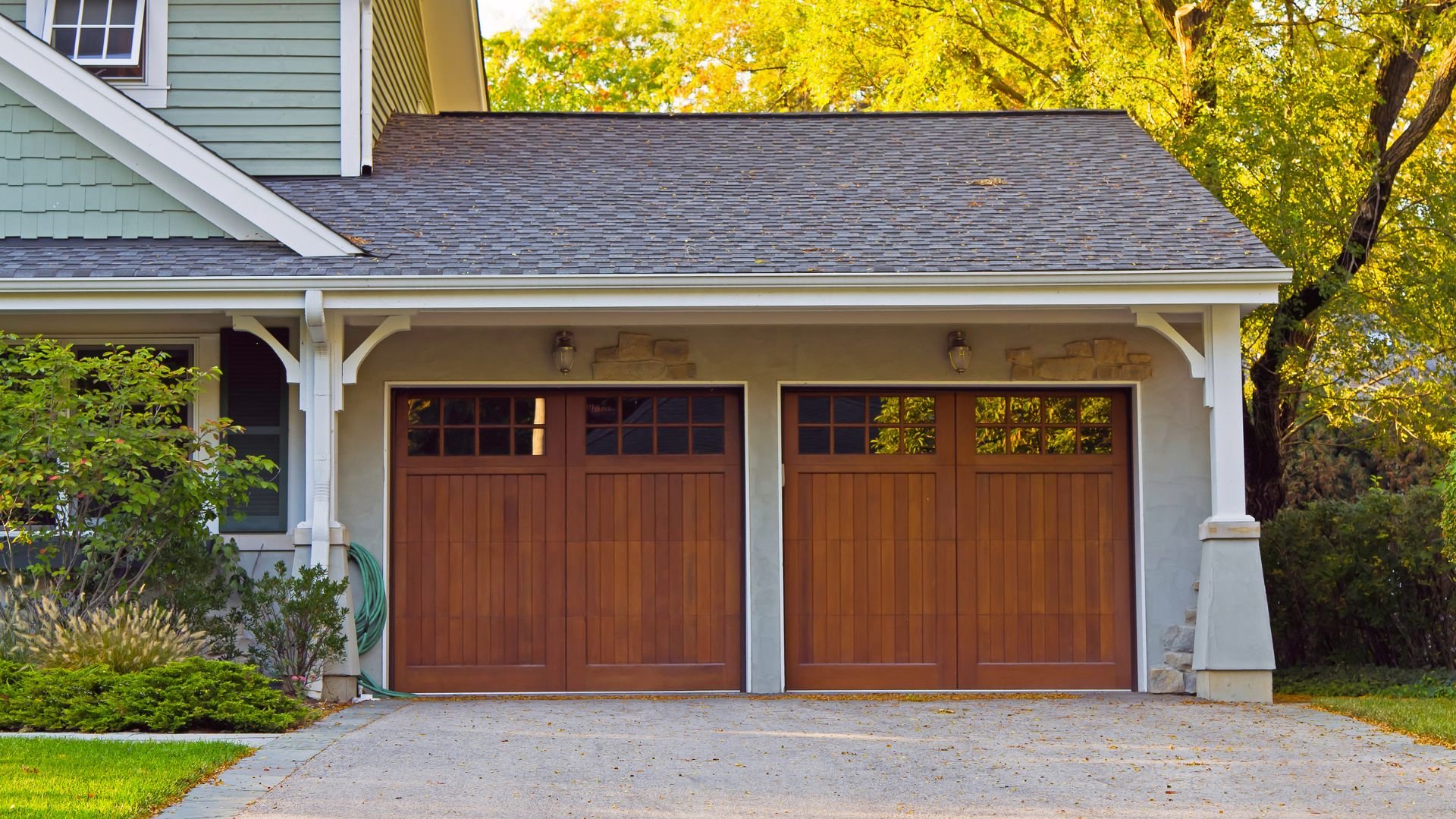 Wooden double garage doors on a green house with autumn trees